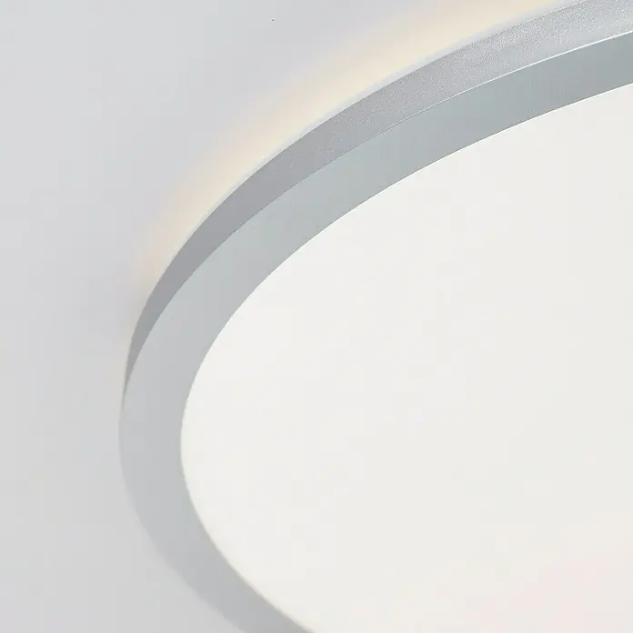 Brilliant LED-Deckenleuchte rund Tanida - 46 W, Ø x H: 57 x 3,2 cm, Silber, RGBW - Nahaufnahme einer modernen, runden LED-Deckenleuchte mit silberfarbenem Rahmen, die ein helles, indirektes Licht erzeugt.
