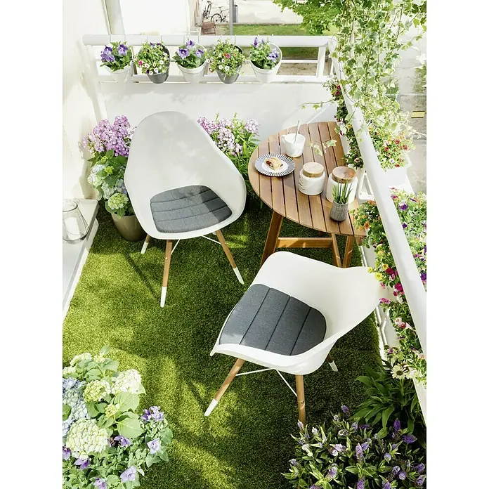 Sunfun Diana Balkontisch - L x B x H: 100 x 50 x 75 cm, Akazie, Klappbar, Gebogen, Naturbraun - Blick auf einen Balkon mit zwei Stühlen, einem Tisch und vielen Pflanzen.