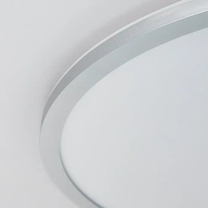 Brilliant LED-Deckenleuchte rund Tanida - 46 W, Ø x H: 57 x 3,2 cm, Silber, RGBW - Nahaufnahme einer runden LED-Deckenleuchte mit silbernem Rahmen und weißem Diffusor, die ein modernes und minimalistisches Design aufweist.