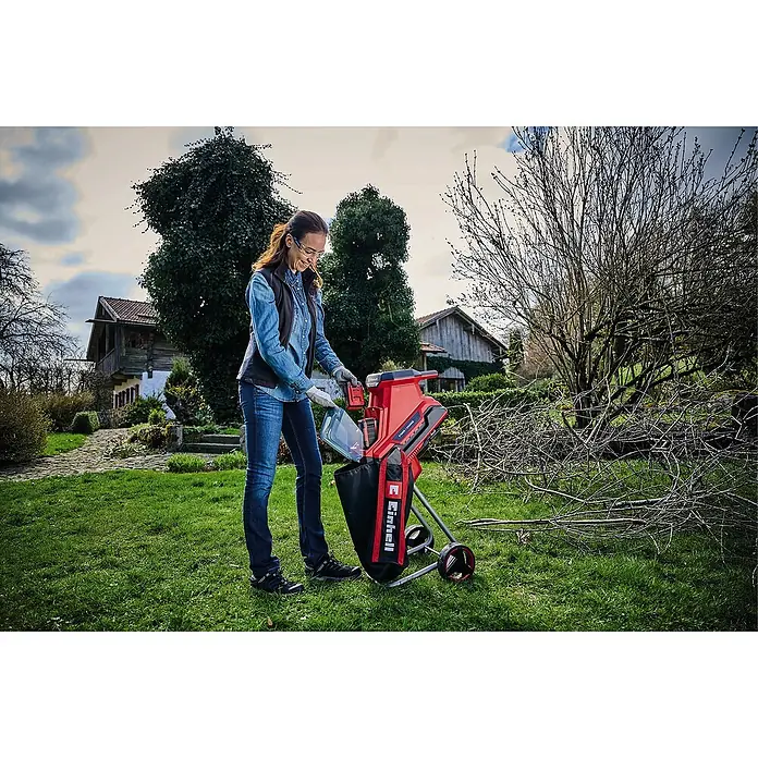 Einhell Power X-Change 18V Akku-Häcksler Redaxxo 36/25 - Max. Aststärke: 2,5 cm - Frau benutzt einen roten Einhell Gartenhäcksler im Garten, um Äste zu zerkleinern.
