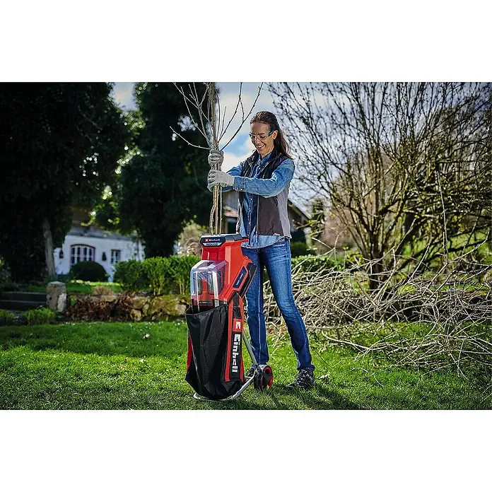 Einhell Power X-Change 18V Akku-Häcksler Redaxxo 36/25 - Max. Aststärke: 2,5 cm - Eine Frau bedient einen Einhell-Gartenhäcksler im Freien, um Äste zu zerkleinern. Praktisches Gartengerät für schnelles Aufräumen.