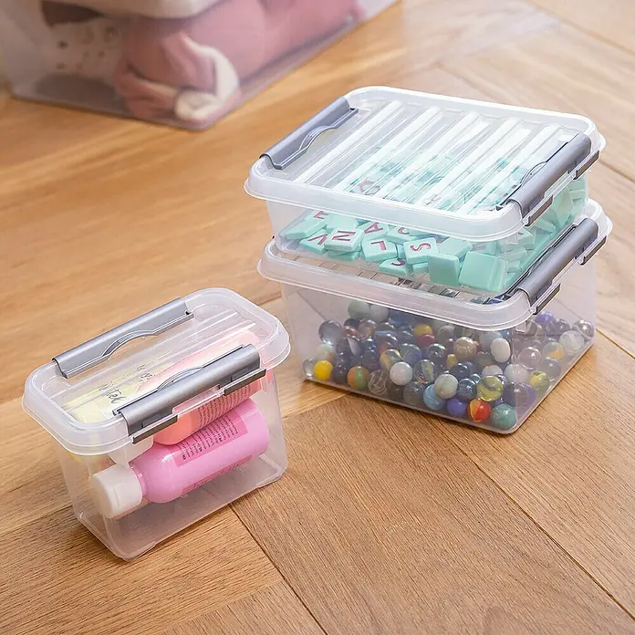 Sunware Aufbewahrungsbox Q-Line - L x B x H: 20 x 15 x 6 cm, Kunststoff, Transparent, Farbe Griff: Schwarz - Klarer Aufbewahrungsbehälter mit Deckel. Enthält verschiedene Gegenstände zur Aufbewahrung und Organisation auf einem Holzboden.