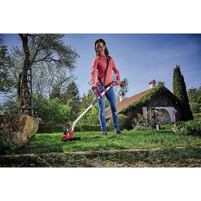 Einhell Power X-Change 18V Akku-Rasentrimmer GE-CT 18/33 Li-Solo - 18 V, Li-Ionen, Ohne Akku - Frau, die einen Einhell Akku-Rasentrimmer im Garten verwendet, mit einem Haus im Hintergrund.