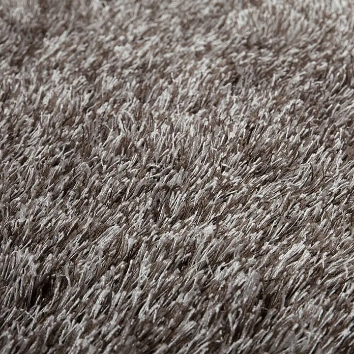 Kayoom Hochflorteppich Diamond - Champagner, 230 x 160 cm, 100 % Polyester - Detailaufnahme eines weichen, grauen Shaggy-Teppichs. Die langen Fasern erzeugen eine gemütliche und einladende Textur, ideal für Wohnräume.