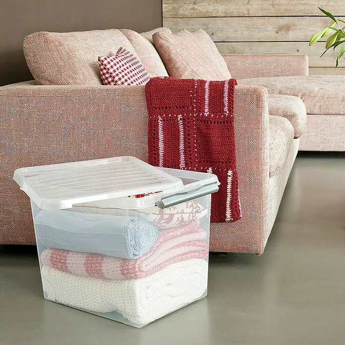 Sunware Aufbewahrungsbox Q-Line - L x B x H: 50 x 40 x 38 cm, Kunststoff, Transparent, Farbe Griff: Schwarz - Aufbewahrungsbox mit Decken und Deckel. Die transparente Box steht vor einem Sofa und enthält ordentlich gefaltete Textilien.