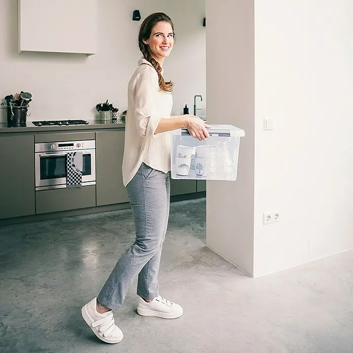 Sunware Aufbewahrungsbox Q-Line - L x B x H: 50 x 40 x 26 cm, Kunststoff, Transparent, Farbe Griff: Schwarz - Frau trägt eine transparente Aufbewahrungsbox mit Deckel, ideal für die Organisation und Lagerung von Gegenständen im Haushalt.