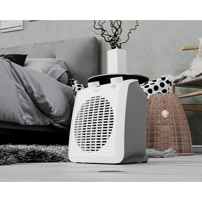 Voltomat HEATING Heizlüfter - 1.000 W - 2.000 W, Weiß/Grau, 19,5 x 14,9 x 23 cm - Nahaufnahme eines tragbaren Heizlüfters mit weißem Gitter und grauen Seitenwänden in einem gemütlichen Schlafzimmer.