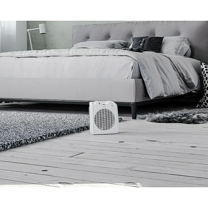Voltomat HEATING Heizlüfter - 1.000 W - 2.000 W, Weiß/Grau, 19,5 x 14,9 x 23 cm - Weißer, tragbarer Heizlüfter steht auf einem Holzboden vor einem grauen Teppich und einem Bett.