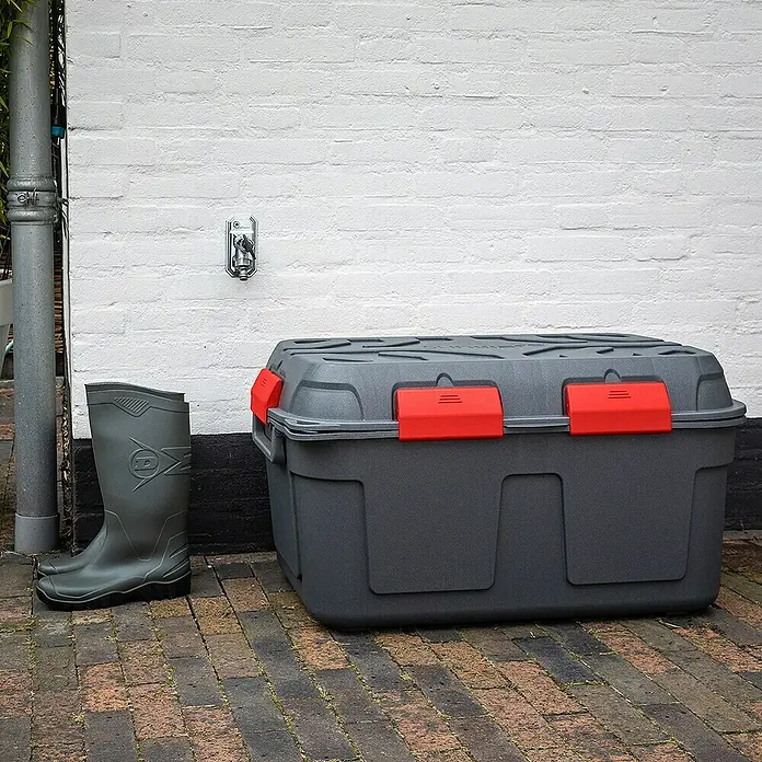 Sunware Aufbewahrungsbox Q-Line - L x B x H: 79 x 54,5 x 42,5 cm, Kunststoff, Anthrazit - Graue Aufbewahrungsbox mit roten Verschlüssen, ideal für den Außenbereich, neben Gummistiefeln auf einer Terrasse.