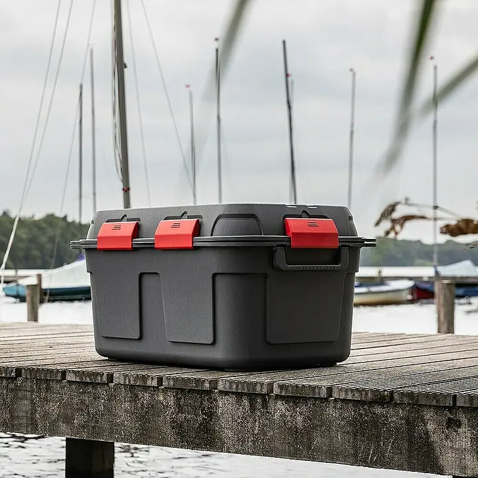 Sunware Aufbewahrungsbox Q-Line - L x B x H: 79 x 54,5 x 42,5 cm, Kunststoff, Anthrazit - Schwarze Aufbewahrungsbox mit roten Verschlüssen auf einem Holzsteg mit Segelbooten im Hintergrund. Ideal für Outdoor-Aktivitäten.