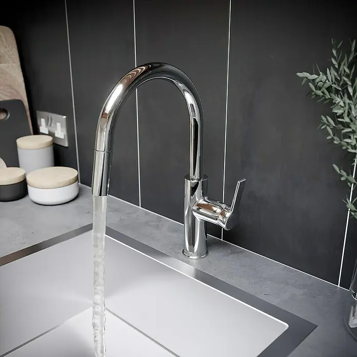 Lenz Spültischarmatur Anela - Chrom, Glänzend - Der elegante, verchromte Wasserhahn mit hohem Auslauf fließt in ein modernes Waschbecken, das durch die dunkle Fliesenwand einen stilvollen Kontrast bietet.