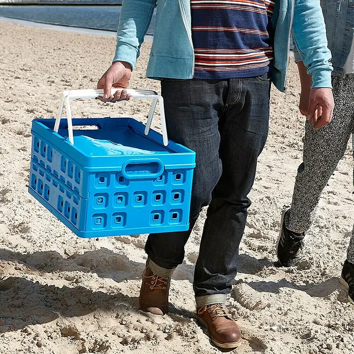 Sunware Kühltasche - L x B x H: 490 x 360 x 250 mm, Fassungsvermögen: 32 l - Blaue faltbare Einkaufskiste mit weißem Griff, getragen von einer Person am Strand. Praktisch für unterwegs!