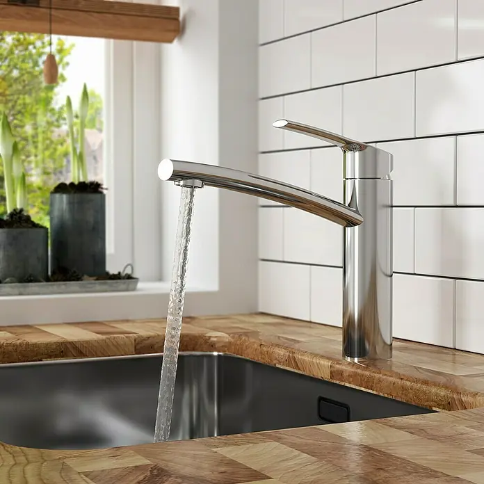 Lenz Spültischarmatur Kimo - Chrom, Glänzend - Ein moderner Chrom-Wasserhahn mit fließendem Wasser in einem stilvollen Küchendesign mit Holzoberfläche und weißen Fliesen.