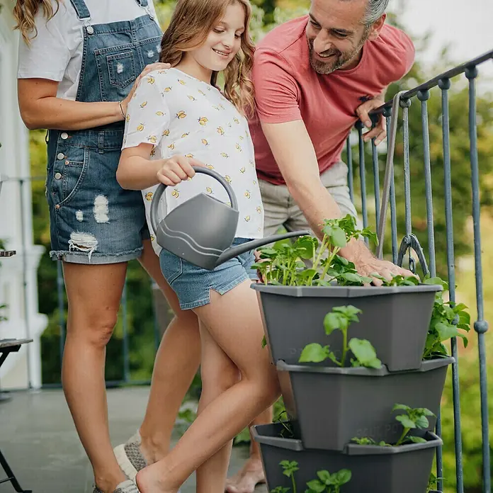 Gusta Garden Pflanzturm Paul Potato - 44 x 44 x 65 cm, Anthrazit - Familie gießt Pflanzen in einem vertikalen PaulPot Pflanzgefäß auf dem Balkon, das eine platzsparende Lösung bietet.