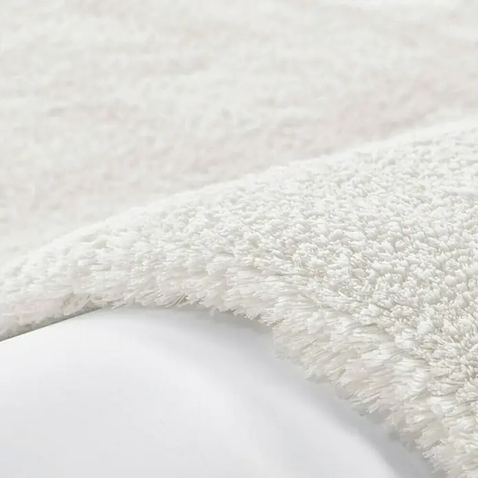 Kayoom Hochflorteppich Bali - Elfenbein, 150 x 80 cm, 100 % Polyester - Detailaufnahme eines flauschigen, weißen Badvorlegers, der auf einer glatten, weißen Oberfläche liegt, ideal für Komfort und Stil im Badezimmer.