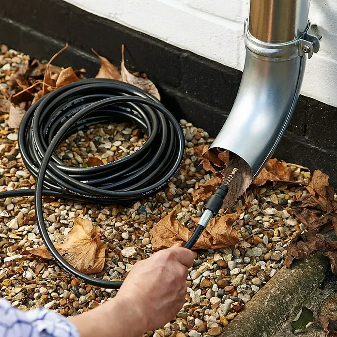 Bosch Verlängerungsschlauch RohrreinigerLänge: 10 m, Passend für: Bosch Hochdruckreiniger Aquatak-Serie - Eine Person reinigt eine Dachrinne mit einem speziellen Reinigungsgerät mit schwarzem Schlauch, um Verstopfungen durch Blätter zu beseitigen.