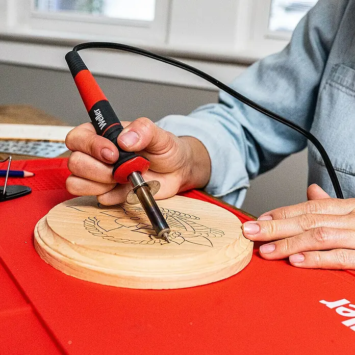 Weller Brandmal-Set WLIWBK2523C - Gesamtumfang: 15 -tlg. - Nahaufnahme einer Person, die mit einem Weller-Brandmalkolben ein Holzstück bearbeitet, um ein detailliertes Design zu erstellen.