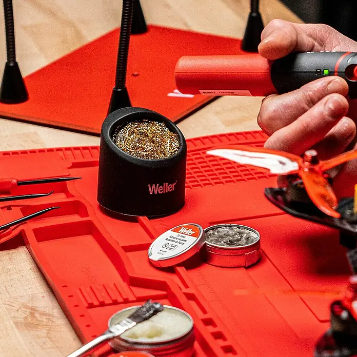 Weller Lötspitzenreiniger WLACCBSH-02mit Silikon-Ablage - Geeignet für: Lötarbeiten, 2 -tlg. - Ein Weller-Lötzubehör-Set auf einer roten Arbeitsmatte, inklusive Lötzinn, Flussmittel und Reinigungsutensilien.