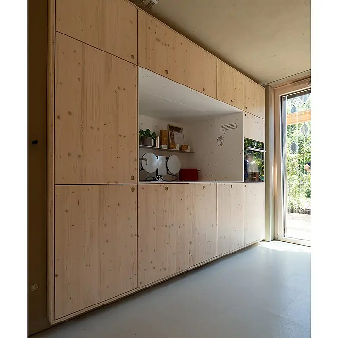 elka 3-Schichtplatte Vita - Fichte, 2.500 x 660 x 19 mm - Eine Küchenzeile aus hellem Holz mit zahlreichen Schränken und integrierten Geräten. Offenes Fach mit Deko und ein Einbaubackofen ergänzen die Küchenzeile.
