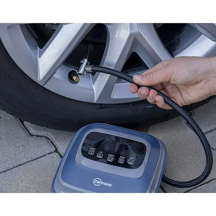 Cartrend Luftpumpe - 10 bar, 12 V - Eine Person füllt einen Reifen mit einem digitalen cartrend-Luftkompressor auf, der auf Pflastersteinen steht.