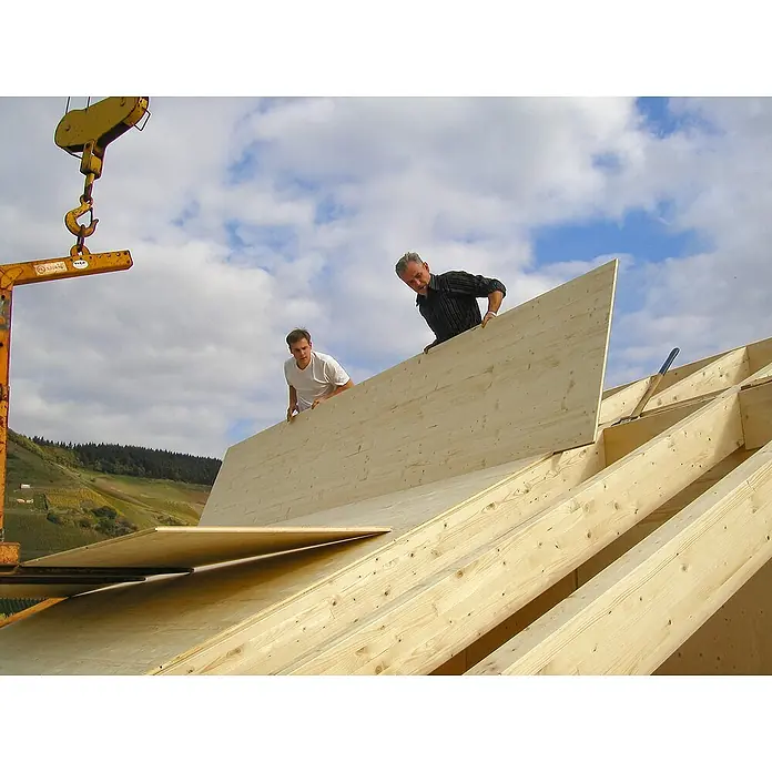 elka 3-Schichtplatte Vita - Fichte, 2.500 x 660 x 19 mm - Zwei Bauarbeiter montieren Holzplatten auf einem Dachstuhl, wobei ein Kran im Hintergrund die Platten liefert. Die helle Holzkonstruktion dominiert.