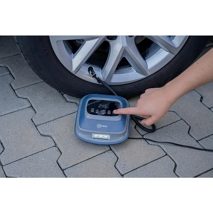 Cartrend Luftpumpe - 10 bar, 12 V - Eine Hand bedient eine digitale Cartrend-Luftpumpe neben einem Reifen, um den Reifendruck präzise einzustellen.