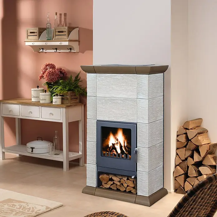 Domofire Kaminofen Cortina - 8 kW, Raumheizvermögen: 160 m³, Material Verkleidung: Keramik, Cremebeige-Tabakbraun - Ein stilvoller Kaminofen mit Holzfächern, umgeben von rustikalen Möbeln, strahlt Wärme und Behaglichkeit aus. Perfekt für gemütliche Abende.