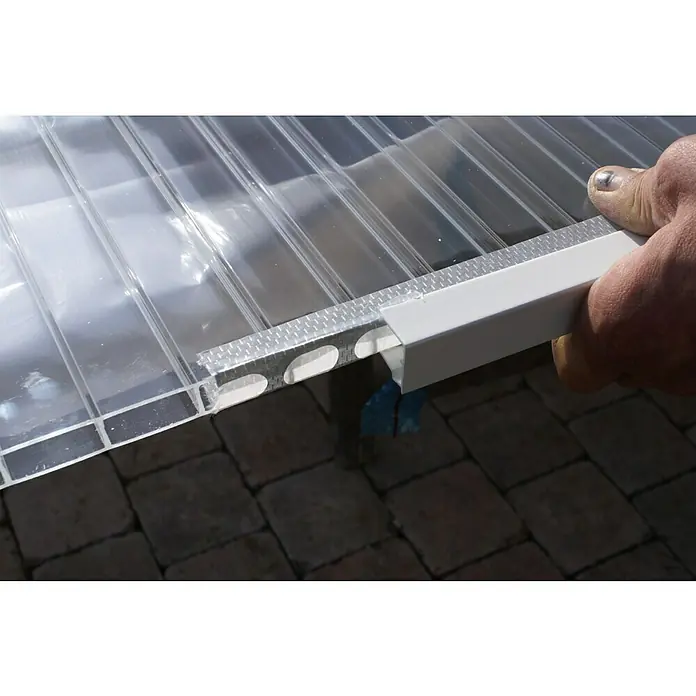 Abschlussprofil - 98 cm x 16 mm, Weiß, Geeignet für: Stegplatten 16 mm, Aluminium - Ein Mann befestigt ein weißes U-Profil an einer transparenten Mehrfachstegplatte, die auf einem gepflasterten Untergrund liegt.