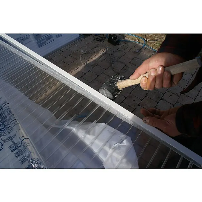 Abschlussprofil - 98 cm x 16 mm, Weiß, Geeignet für: Stegplatten 16 mm, Aluminium - Ein Arbeiter befestigt eine durchsichtige Polycarbonatplatte mit einem Gummihammer an einem weißen Rahmen. Die Platte ist teilweise mit Folie bedeckt.