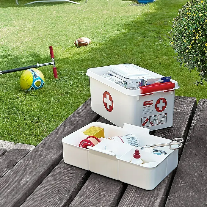 Sunware Erste-Hilfe-Box Q-Line - L x B x H: 30 x 20 x 14 cm, Kunststoff - Erste-Hilfe-Kasten mit Medikamenten und medizinischem Zubehör auf einer Holzbank im Garten, bereit für kleine Notfälle.