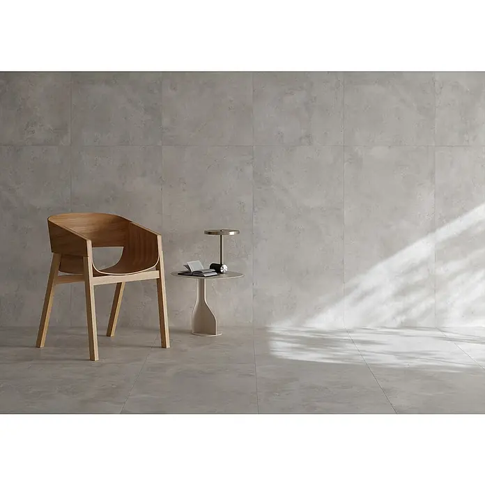 Queens Feinsteinzeugfliese - 79,8 x 79,8 cm, Weiß, Matt - Innenaufnahme mit einem hellen Holzstuhl und einem kleinen Tisch mit Lampe, vor einer Wand mit großformatigen Fliesen. Das Lichtspiel erzeugt eine ruhige Atmosphäre.