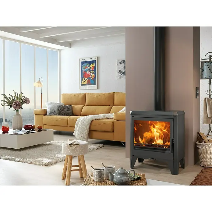Panadero Estufa de leña Nice - 7,4 kW, Volumen de calefacción: 222 m³ - Primer plano de una estufa de leña moderna con llamas visibles, en un espacio de vida elegante con un sofá y decoraciones.