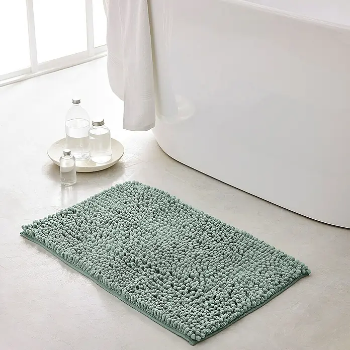 Badteppich Bubble - 45 x 75 cm, Celadon, 100% Polyester - Ein rechteckiger, mintgrüner Badteppich mit Noppenstruktur liegt vor einer weißen Badewanne und einer Fensterfront.