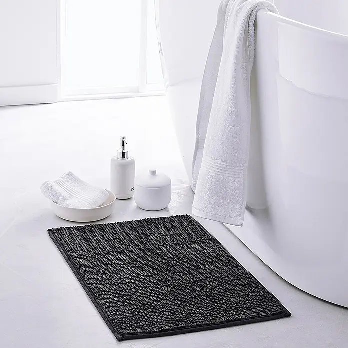 Badteppich Bubble - 40 x 60 cm, Schwarz, 100% Polyester - Ein grauer Badteppich liegt vor einer weißen Badewanne, neben weißen Handtüchern und Badezimmeraccessoires.