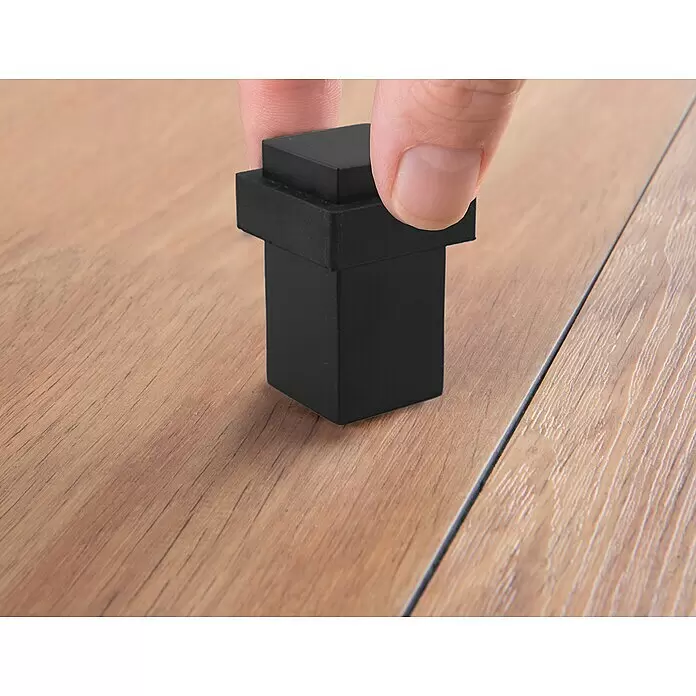 Walteco Bodentürstopper - L x B x H: 20 x 20 x 48 mm, Metall - Hand platziert schwarzen, rechteckigen Baustein auf Holztisch.