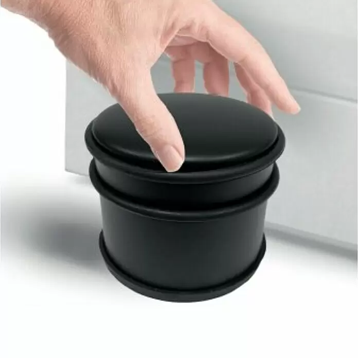 Walteco Bodentürstopper - Ø x H: 95 x 75 mm, Metall - Schwarzer zylindrischer Türstopper mit Gummiringen, der vor einer weißen Tür platziert wird.