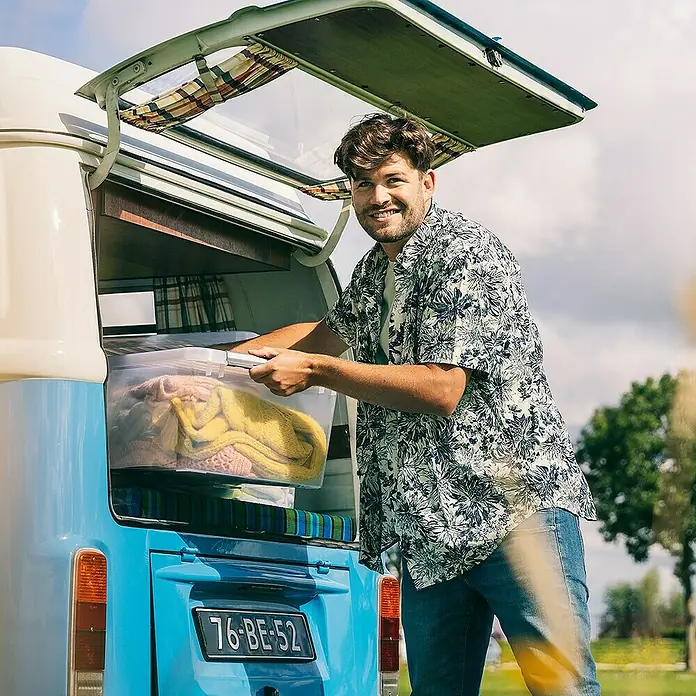 Sunware Aufbewahrungsbox Q-Line - L x B x H: 60 x 40 x 26 cm, Kunststoff, Transparent, Farbe Griff: Schwarz - Mann verstaut durchsichtige Kunststoffbox mit Strickwaren in einem blauen VW-Bus.