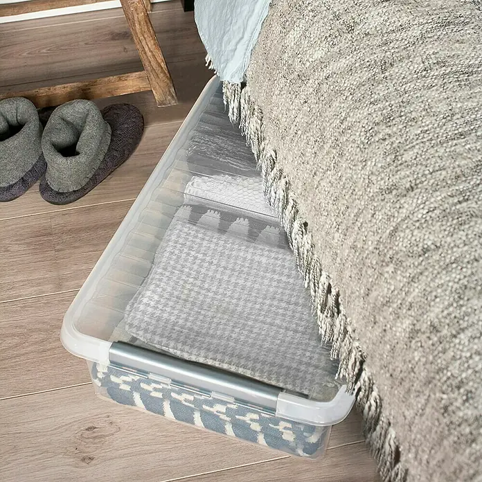 Sunware Aufbewahrungsbox Q-Line - L x B x H: 60 x 40 x 18 cm, Kunststoff, Transparent, Farbe Griff: Schwarz - Eine transparente Aufbewahrungsbox mit verschiedenen Textilien darunter auf einem Holzboden, die unter einem Bett steht.