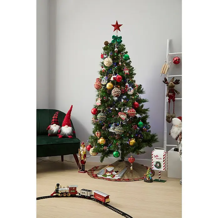 Figura decorativa Bjorn - Textil - Árbol de Navidad decorado festivamente con estrella roja, adornos y luces, rodeado de decoraciones navideñas como un tren y gnomos.