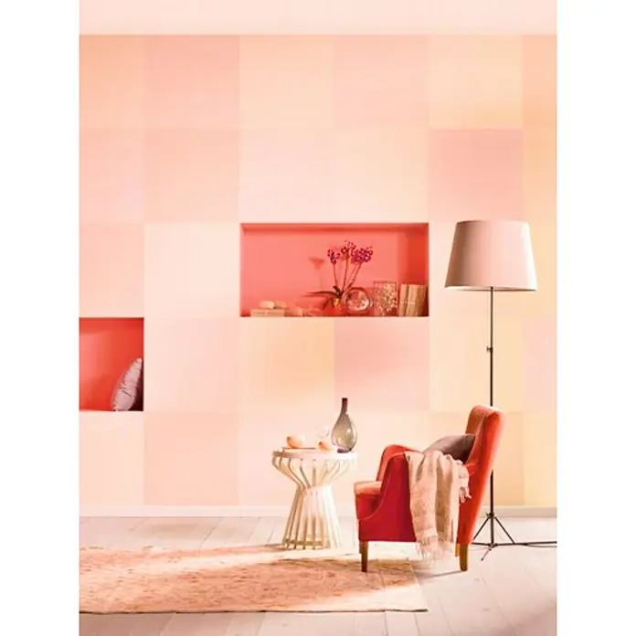 Bruguer Colores del Mundo Pintura para paredes - India melocotón suave, Mate, 4 l - Acogedora sala de estar con sillón rojo, mesa auxiliar y lámpara de pie frente a una pared con bloques de color cuadrados y nichos.