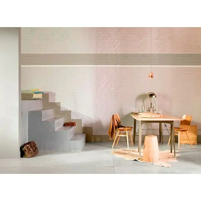 Bruguer Colores del Mundo Pintura para paredes - Patagonia perla suave, Mate, 4 l - Acogedora zona de comedor con mesa de madera, sillas y una alfombra decorativa en una elegante habitación con escalera y pared de ladrillo.