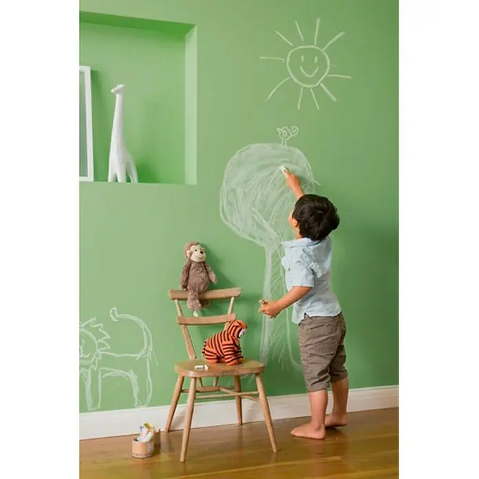 Bruguer Ultra Resist Pintura para paredes - Verde envejecido, Mate, 4 l - Un niño dibuja con tiza en una pared verde, y un mono y un tigre están sentados en una silla de madera.