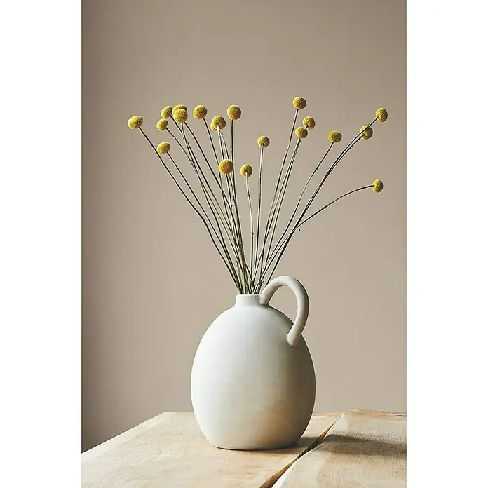 Alpina Wandfarbe Feine Farben - Wiege des Aromas, Matt, 2,5 l, Konservierungsmittelfrei - Eine Nahaufnahme einer Vase mit gelben Craspedia-Blumen, die auf einem Holztisch steht und eine elegante und schlichte Dekoration darstellt.