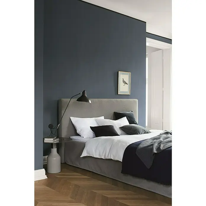 Alpina Wandfarbe Feine Farben - Himmlische Nachtmusik, Matt, 2,5 l, Konservierungsmittelfrei - Elegantes Schlafzimmer mit einem grauen Bett, weißen Kissen und einer schwarzen Lampe auf einem Nachttisch. Das Zimmer strahlt eine ruhige Atmosphäre aus.