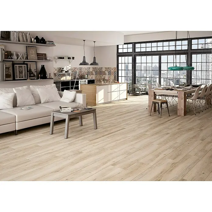 Halcón Pavimento porcelánico Wood - 22,5 x 119,5 cm, Beige, Mate, Rectificado - Amplio salón luminoso con suelo de madera, sofá blanco y zona de comedor bajo grandes ventanales, creando un ambiente acogedor y moderno.