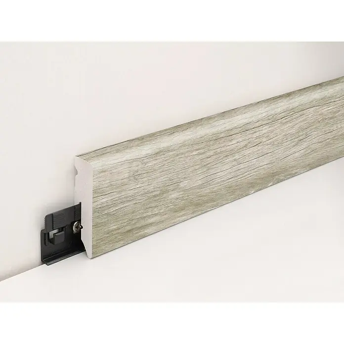 Profiles and more Sockelleiste KU51L Eiche Monza Grau - 240 cm x 15 mm x 50 mm - Nahaufnahme einer stilvollen Fußleiste in Holzoptik mit einem Befestigungssystem an einer weißen Wand.