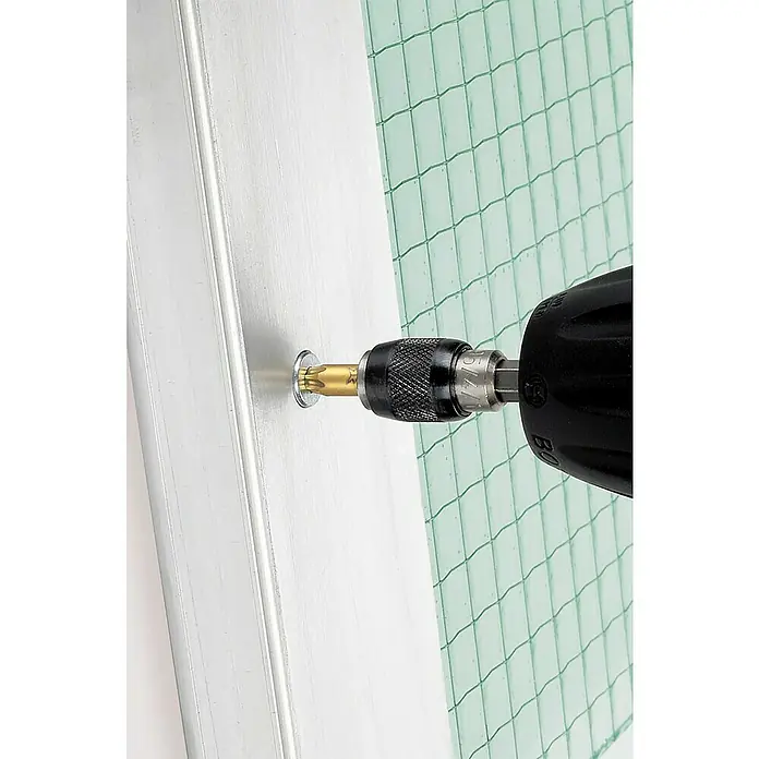 Wolfcraft Diamant-Bit - TX 20 - Ein Akku-Bohrschrauber mit Torx-Bit befestigt eine Schraube in einem silbernen Rahmen, während im Hintergrund ein grünes Netz sichtbar ist.