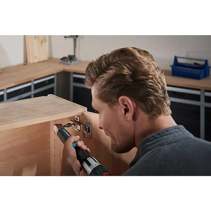 Wolfcraft Bit Solid - 25 mm, 3 Stk., PH 3 - Ein Mann befestigt ein Scharnier an einem Holzschrank mit einem Akku-Bohrschrauber von Wolfcraft, der ein praktisches Zubehörteil hat.