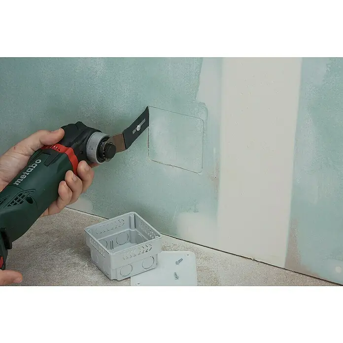 Wolfcraft Tauchsägeblatt Pro mit Tiefenanschlag - 35 mm, 1 Stk. - Ein Metabo-Multifunktionswerkzeug schneidet ein Loch in eine Wand, um eine graue Anschlussdose zu installieren. Deckel und Schrauben liegen daneben.