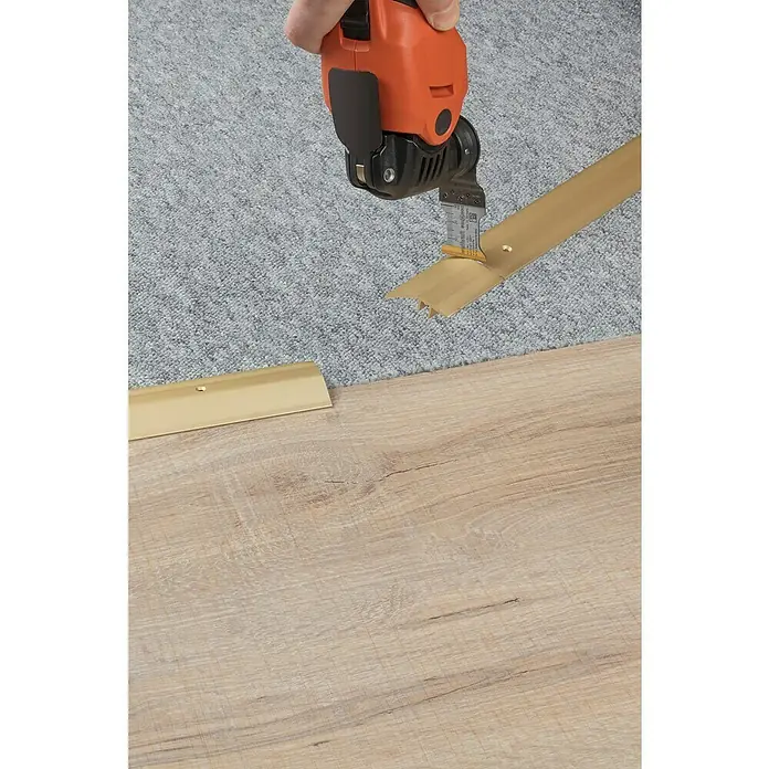 Wolfcraft Tauchsägeblatt HM TiN - 32 mm, 1 Stk. - Ein Elektrowerkzeug schneidet eine goldene Übergangsleiste zwischen einem Teppich und einem Holzboden.